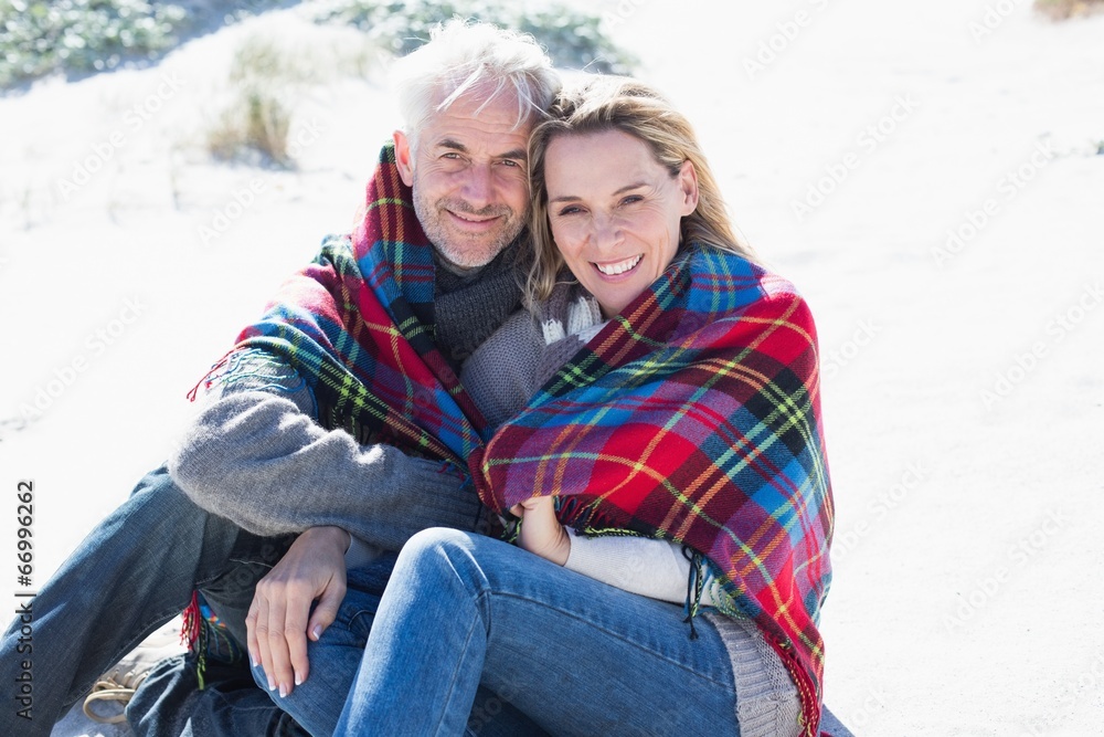 Obraz premium Happy couple wrapped up in blanket sitting on the beach