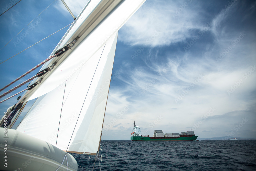Obraz premium Cargo ship on the high seas, in the foreground sail yacht.