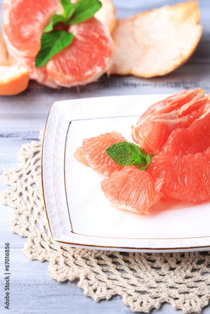 Ripe peeled grapefruits on plate, on color wooden background