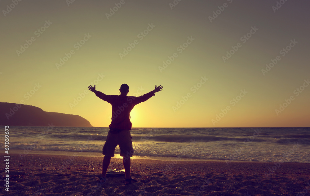 Plakat young man hands up on a beach at sunset