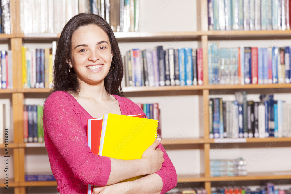 Happy female student holding books at the library Happy female student holding books at the library