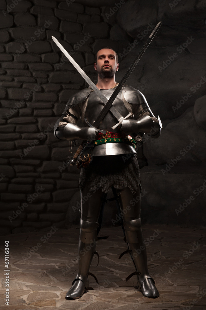 Naklejka premium Medieval Knight posing with two swords on in a dark stone wall b