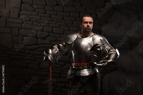 Medieval Knight posing with sword in a dark stone background