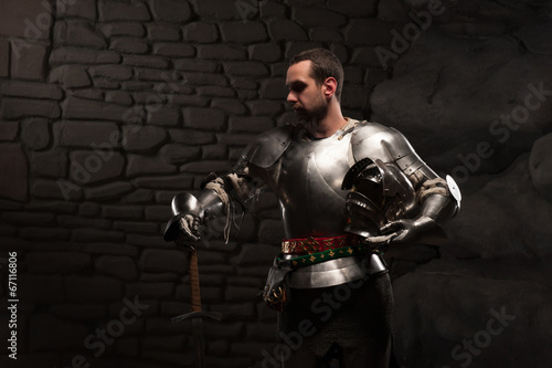 Medieval Knight posing with sword in a dark stone background