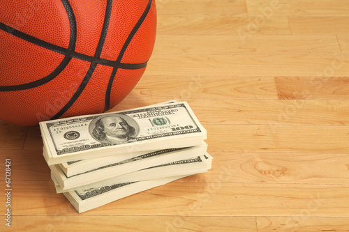 Basketball and one hundred dollar bills on wooden court floor