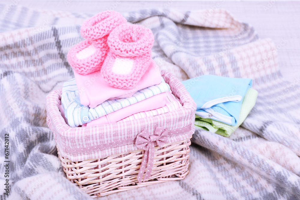Baby clothes in basket on plaid in room Baby clothes in basket on plaid in room