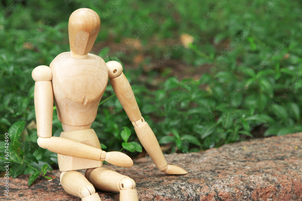Wooden pose puppet sitting on stone, outdoors Wooden pose puppet sitting on stone, outdoors