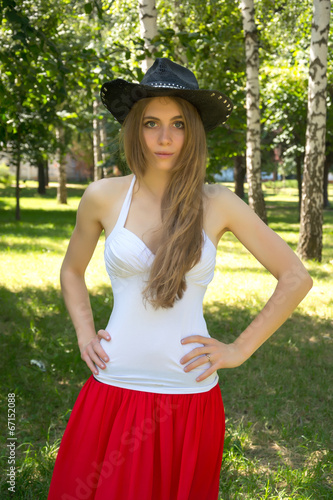 Girl in a cowboy hat and a red skirt in summer park