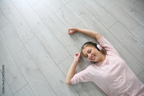 Blond girl relaxing on wooden flooring with headphones on