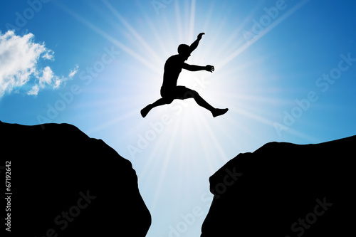 Man jumping over precipice between two rocky mountains