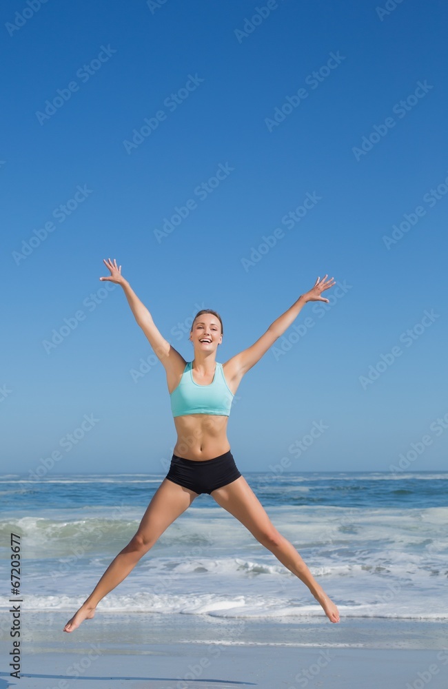 Fit woman jumping on the beach with arms out Fit woman jumping on the beach with arms out
