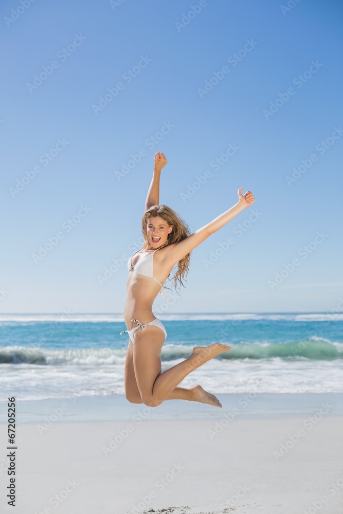 Fit smiling woman in white bikini leaping on beach Fit smiling woman in white bikini leaping on beach