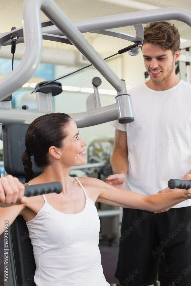 Fit brunette using weights machine for arms with trainer helping Fit brunette using weights machine for arms with trainer helping