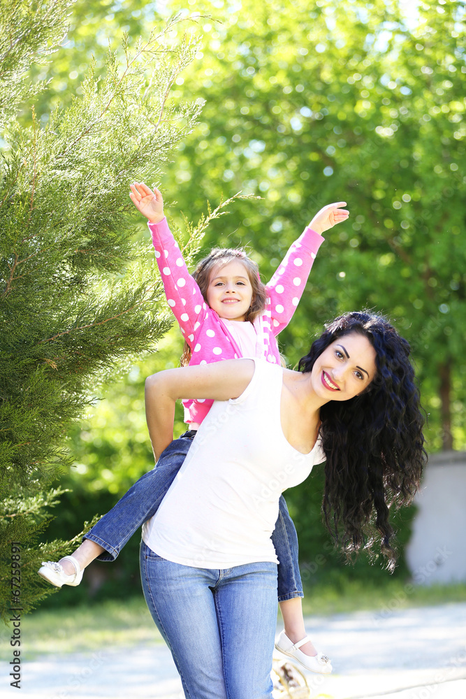 Fototapeta premium Happy mother and daughter piggyback ride in park, family bonding and childhood joy, outdoor recreation and parental love