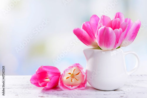 Beautiful tulips in bucket in vase on table on light background