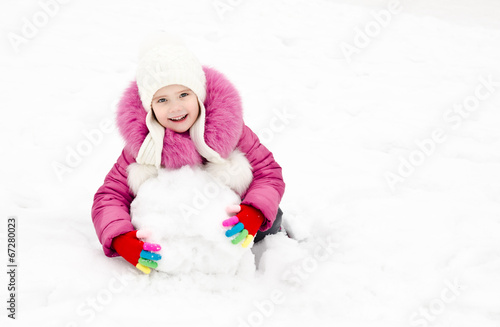 Cute smiling little girl makes snowman in winter day