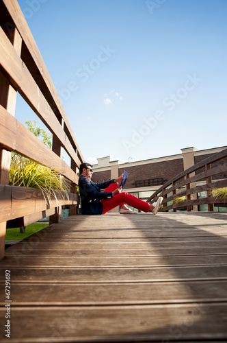 Stylish man sitting on wooden bridge.