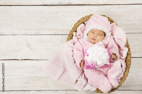 Baby girl with gift sleeping on wooden background, newborn