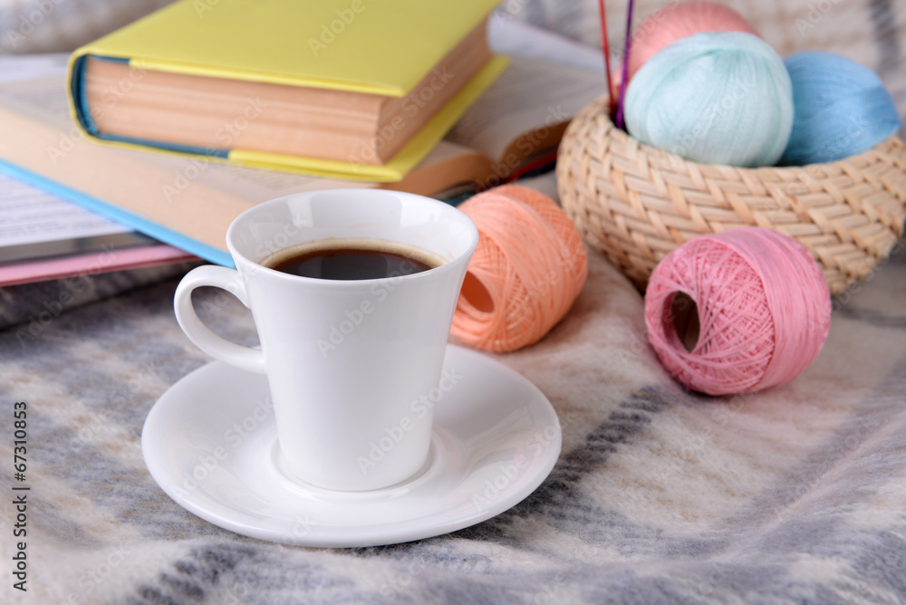 Cup of coffee and yarn for knitting on plaid with books