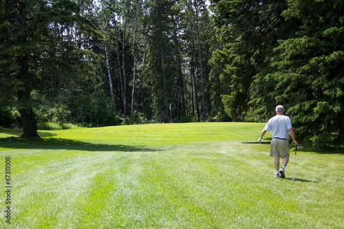 Senior man golfing with flag and greens in sight.