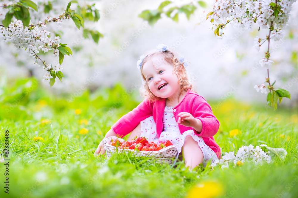 Cute toddler girl eating strawberry in blooming garden Cute toddler girl eating strawberry in blooming garden