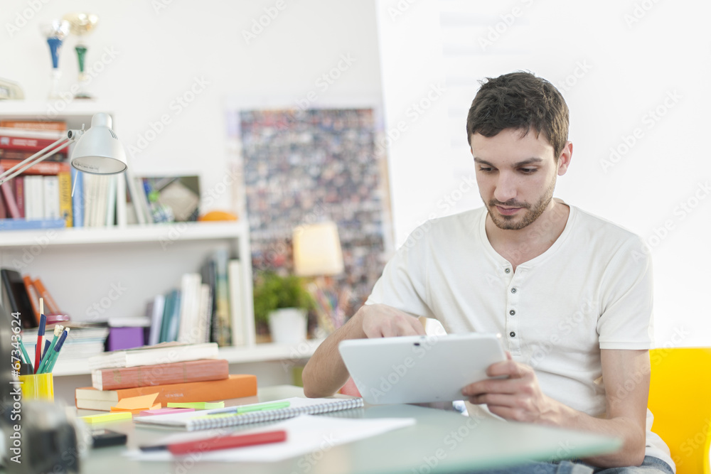 young student sitting at his desk and surfing on a digital table