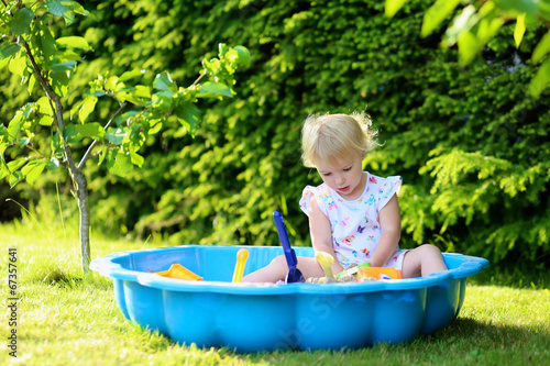 Billede på lærred Happy little girl playing in sandbox in the garden on summer day
