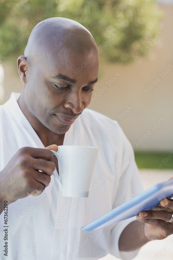 Handsome man in bathrobe using tablet at breakfast outside Handsome man in bathrobe using tablet at breakfast outside