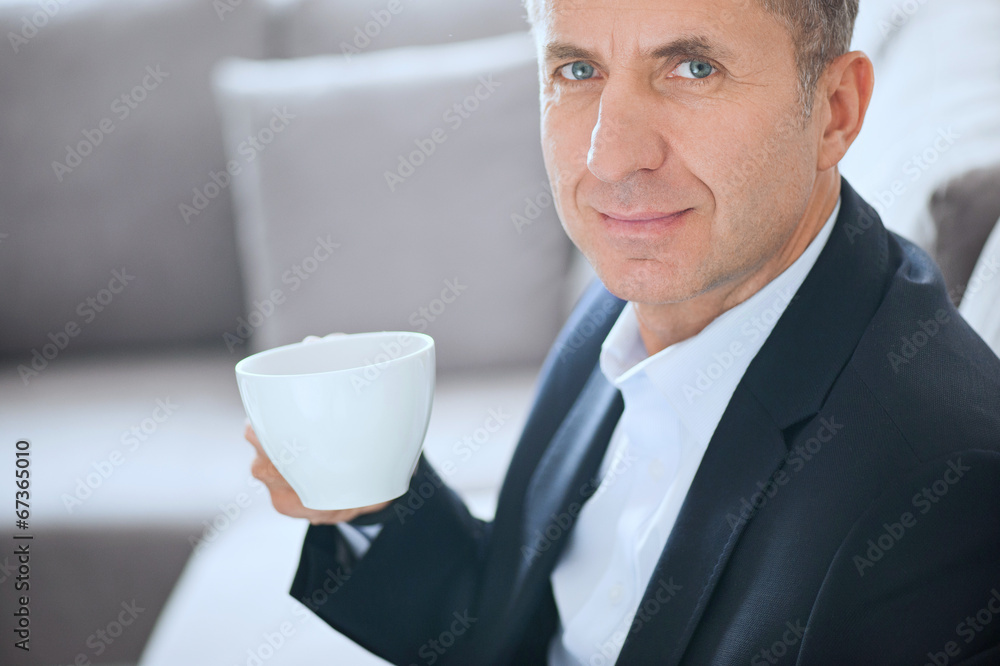 Attractive businessman smiling and drinking a cup of coffee Attractive businessman smiling and drinking a cup of coffee