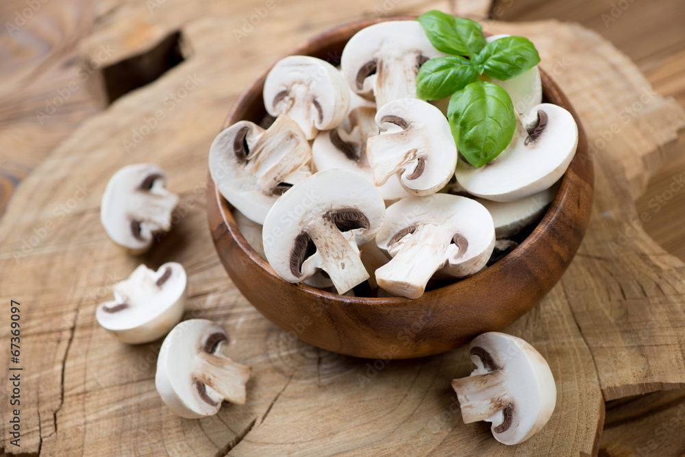 Wooden bowl with raw sliced champignons and green basil Wooden bowl with raw sliced champignons and green basil