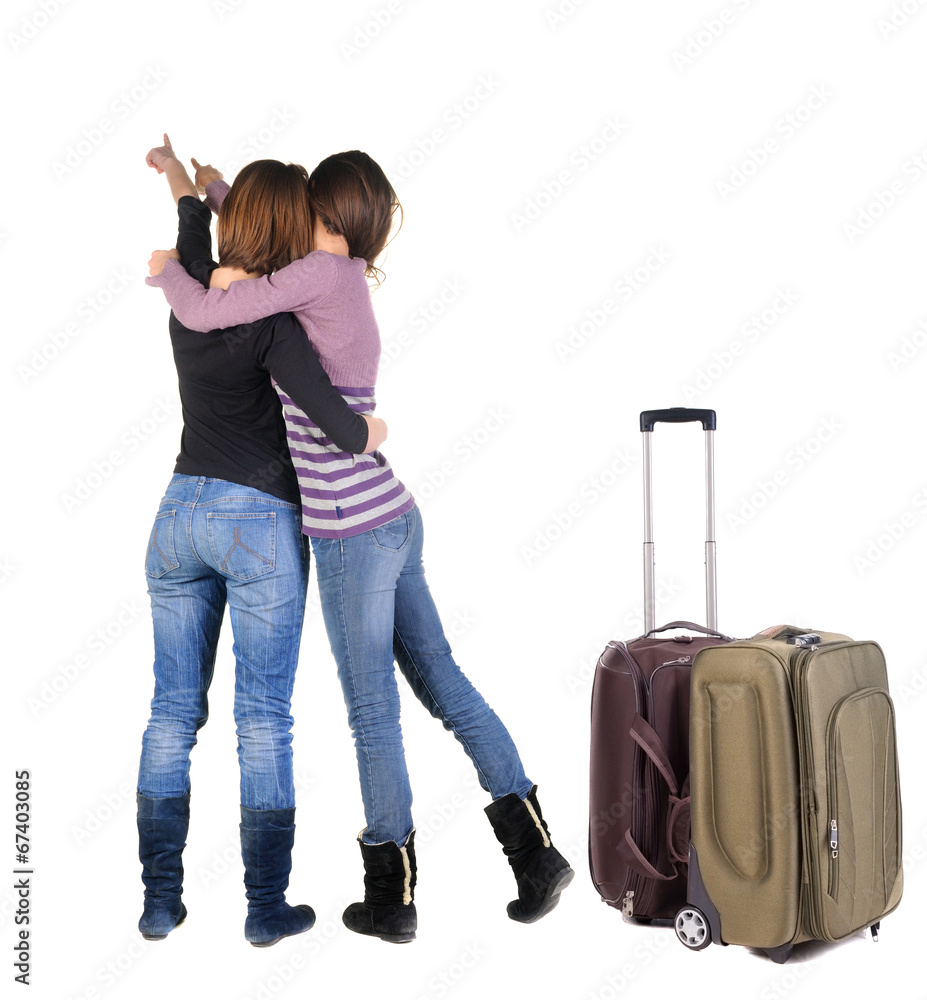 Two women traveling with suitcas and pointing at wall. Two women traveling with suitcas and pointing at wall.