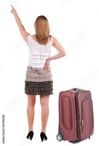 Beautiful young woman in dress traveling with suitcas and pointi