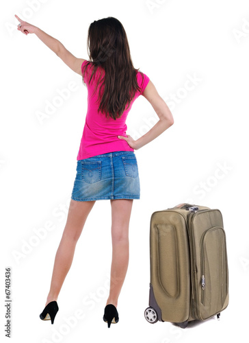 Beautiful young woman in dress traveling with suitcas and pointi