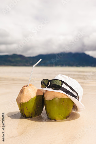 hat and sunglasses with two coco nut cocktails on beach