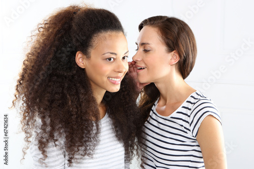 Dwie młode kobiety szepczą sobie do ucha.