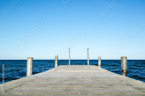 Low angle image of a wooden bath pier in blue water © olandsfokus