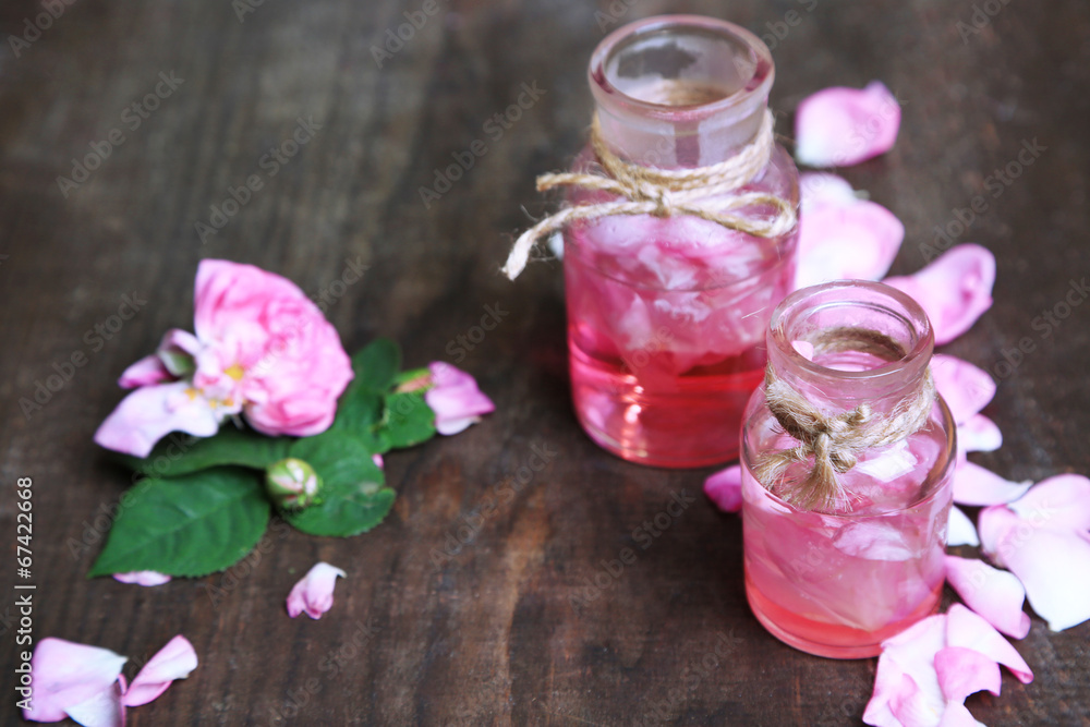 Rose oil in bottles on color wooden background