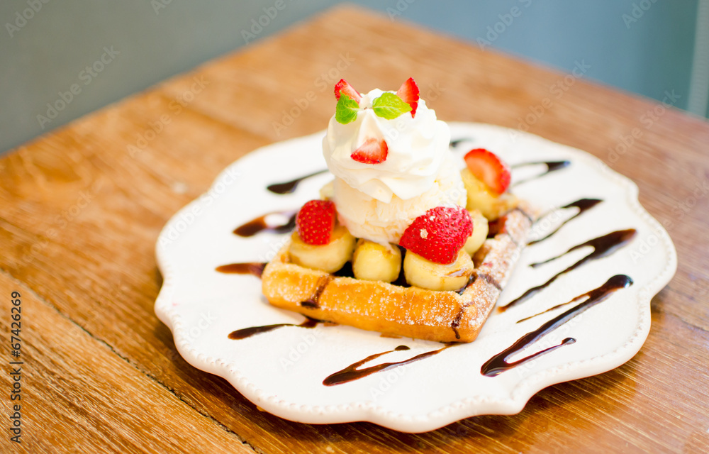 waffle with ice cream topping with strawberry and banana on wood