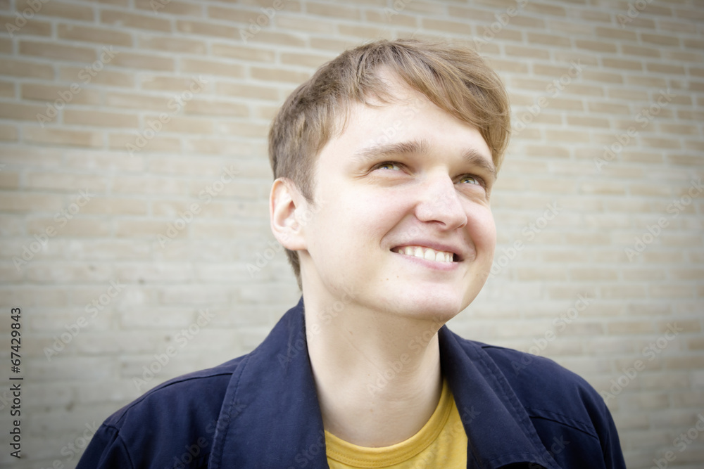 Handsome young man against brick wall smiling. Candid. Handsome young man against brick wall smiling. Candid.