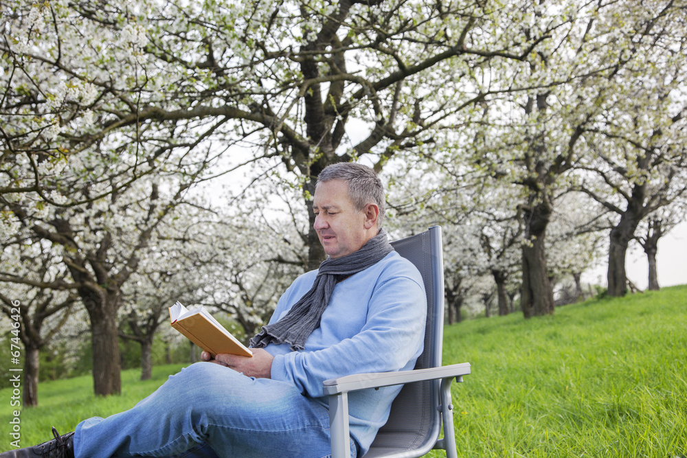 Fototapeta premium Man reading in the book under blooming cherry tree