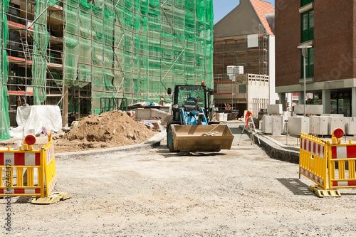 Strassenbauarbeiten vor einem eingerüstetem Neubau