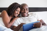 Happy couple cuddling in bed with tablet pc