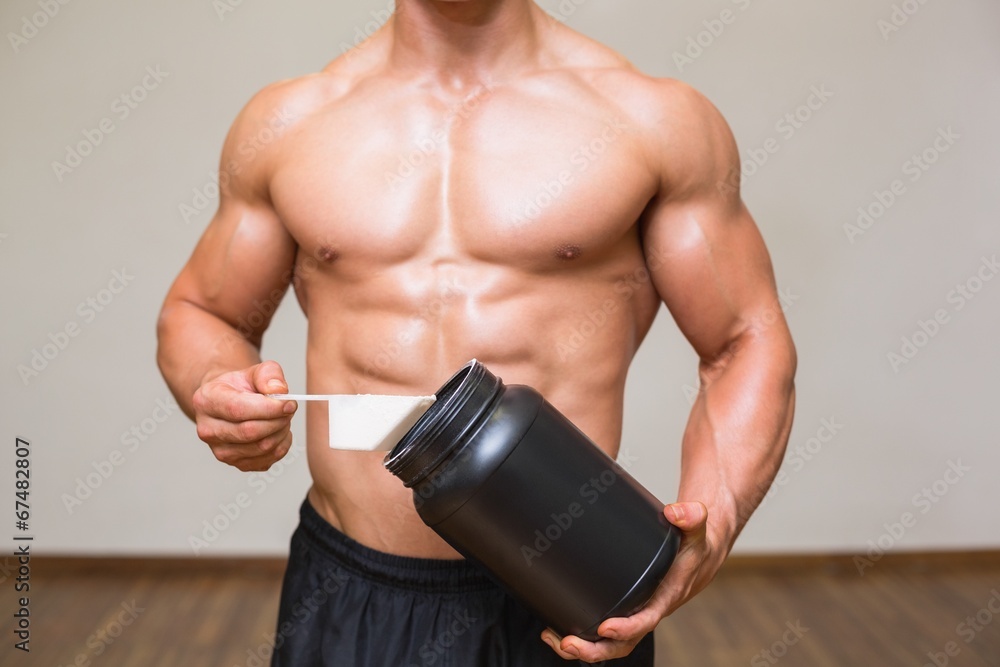 Naklejka premium Body builder holding a scoop of protein mix in gym