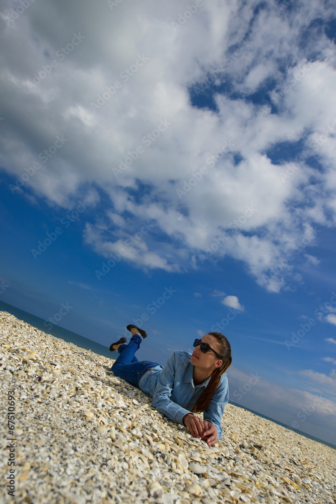 Fototapeta premium Young woman lying on a beach against blue sky on a summer day
