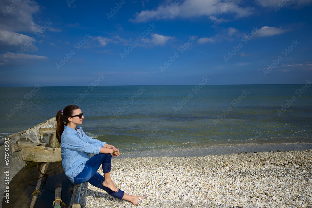 Young woman sitting on a boat at seashore on a summer day