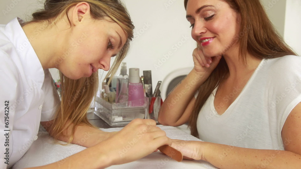 Nail technician filing smiling customers nails Nail technician filing smiling customers nails