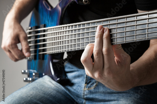 male musician playing on six-string bass guitar