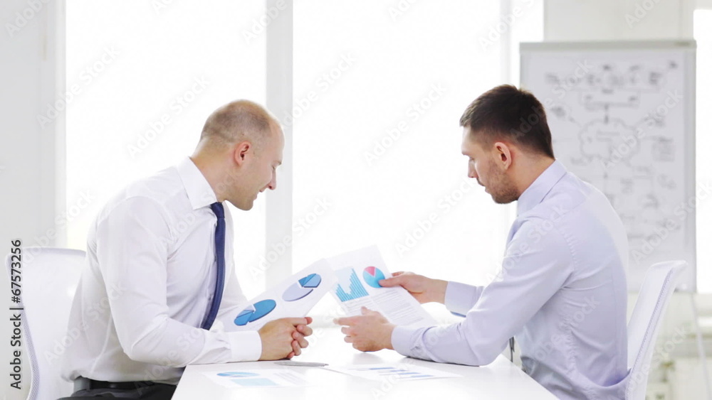 two smiling businessmen with charts in office two smiling businessmen with charts in office