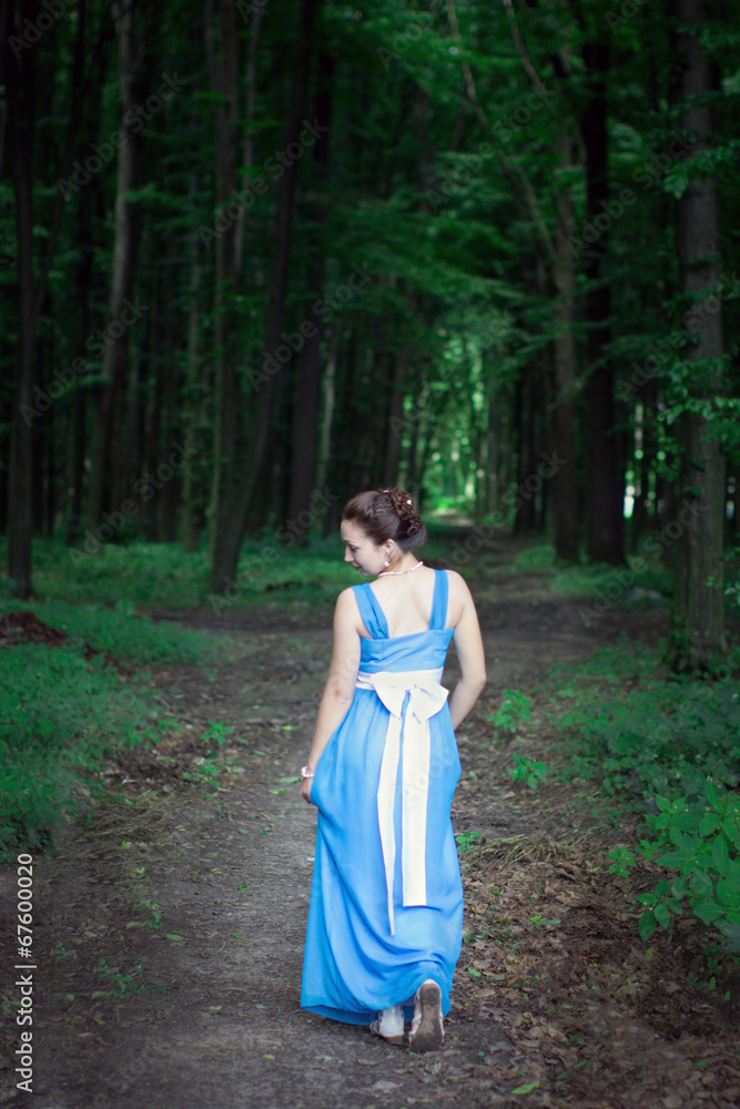 girl in a blue dress walking on the green forest turns around