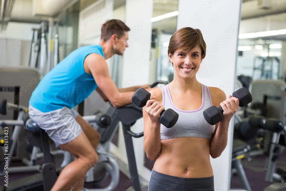 Fit brunette lifting weights smiling at camera Fit brunette lifting weights smiling at camera